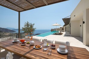 A wooden table set with plates, a vase, and a view of a pool and ocean. - FR Villa Symposium in Sivota (Lefkada)