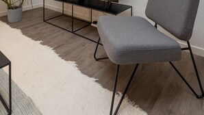 Uma sala de estar moderna com uma televisão de tela plana, uma poltrona cinza, uma mesa de centro e duas plantas em vasos.