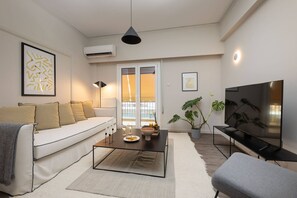 A modern living room with a sofa, coffee table, TV, and potted plant. - Beehive 1B in Athens (Athens)
