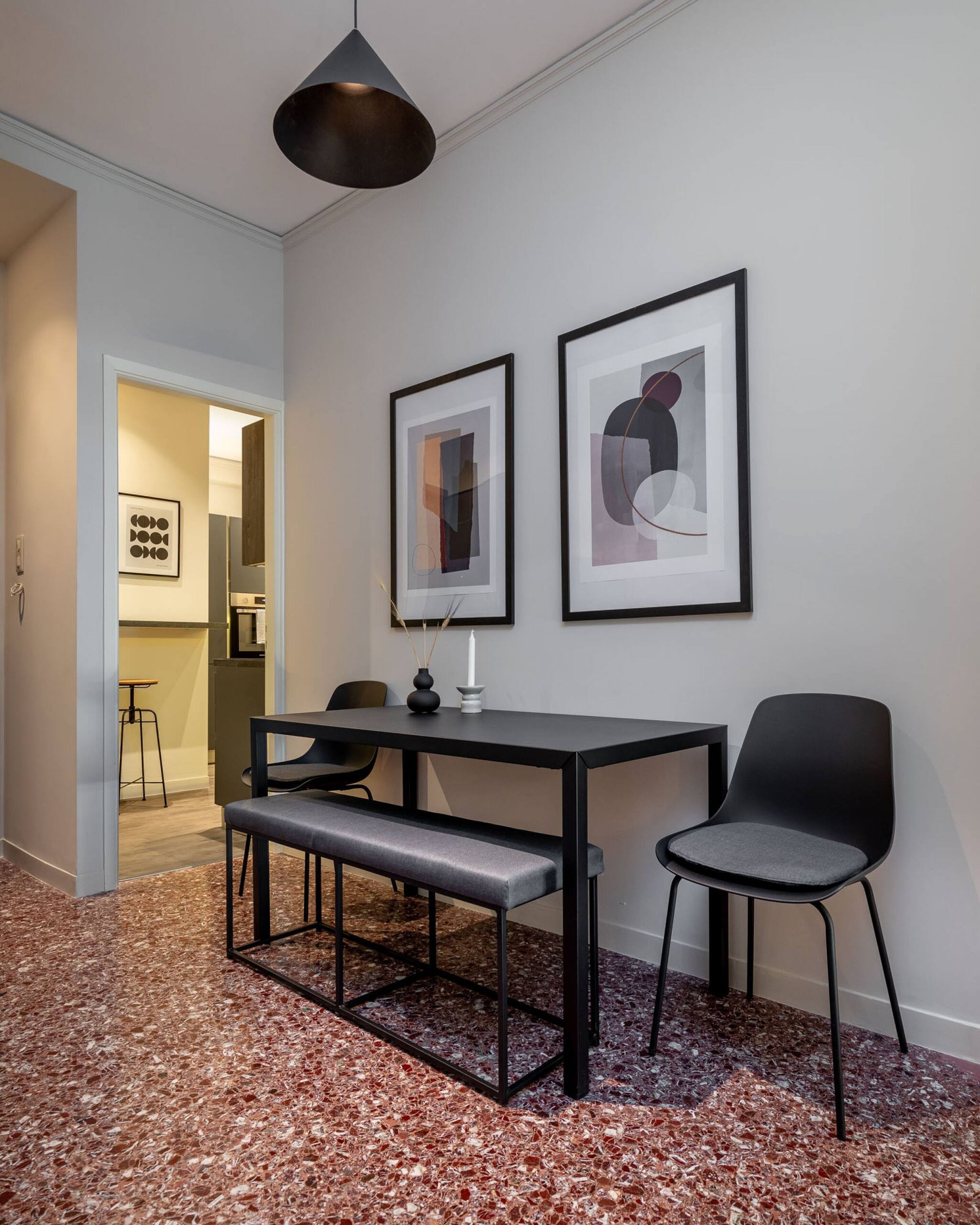 A modern room with a dining table, bench, two chairs, and abstract art on the wall.