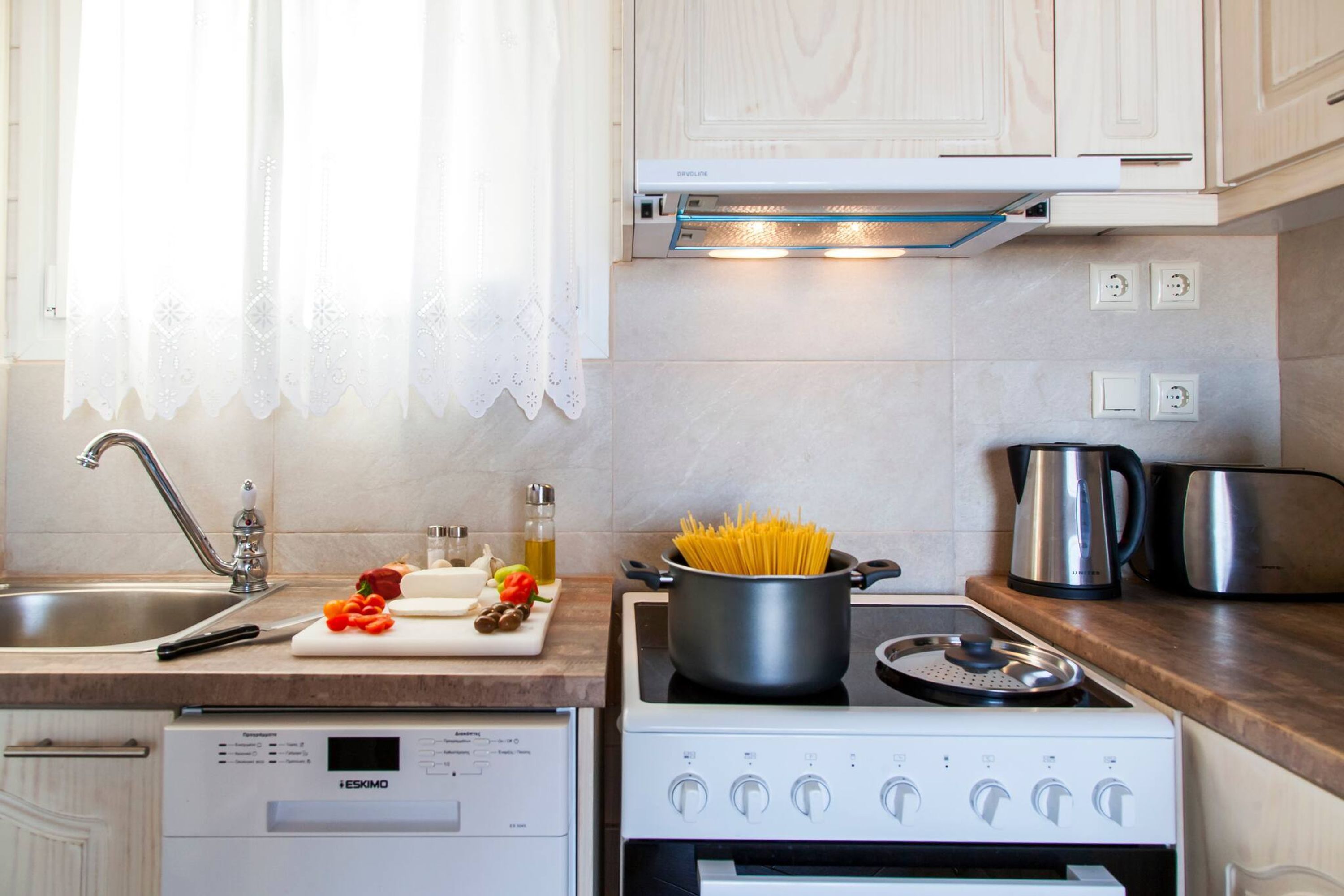A kitchen with a dishwasher, stove, and a pot of spaghetti on the counter.