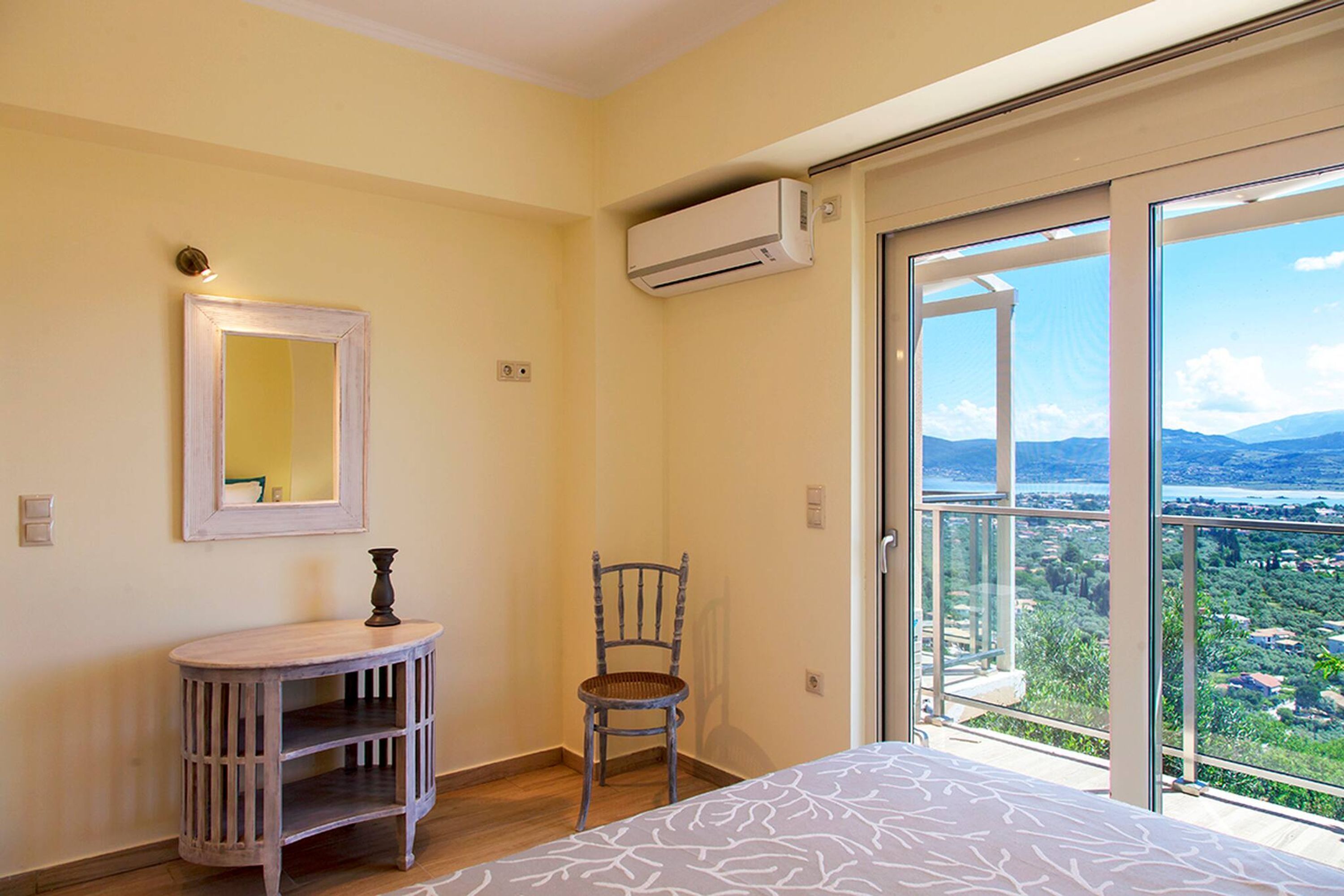 Een slaapkamer met een bed, een stoel, een tafeltje, een spiegel en een balkon met uitzicht.