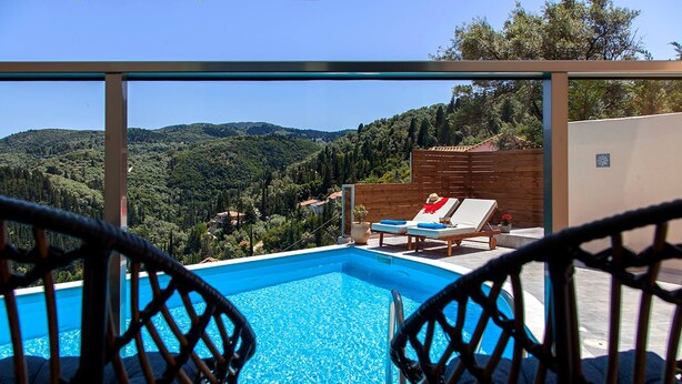 Piscina com duas cadeiras à frente, cercada por um muro de madeira e vista para uma paisagem montanhosa.