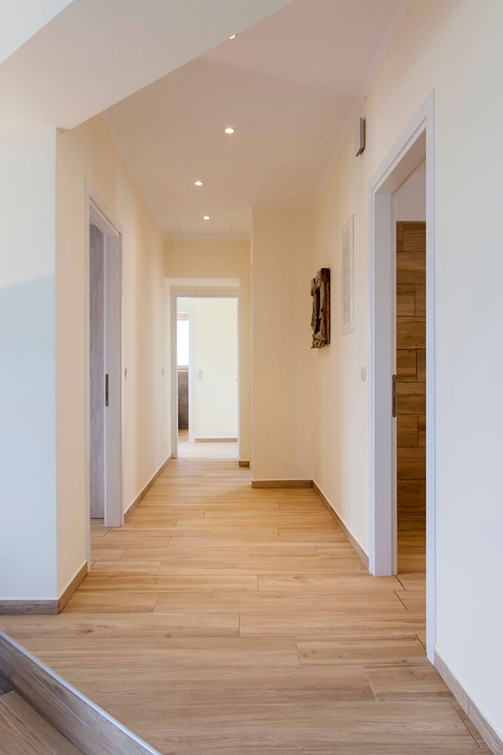 A hallway with wooden flooring, white walls, and a door on the right.