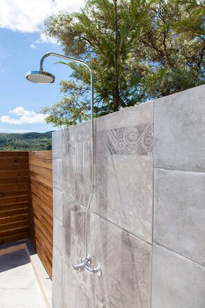 Eine Dusche mit gebogener Brause, ein Holzboden und eine Steinwand mit dekorativem Muster.