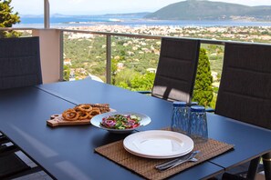A table set for two with a view of a coastal town, a bowl of salad, pretzels, and water bottles. - Villa Alba in Lefkada (Lefkada)