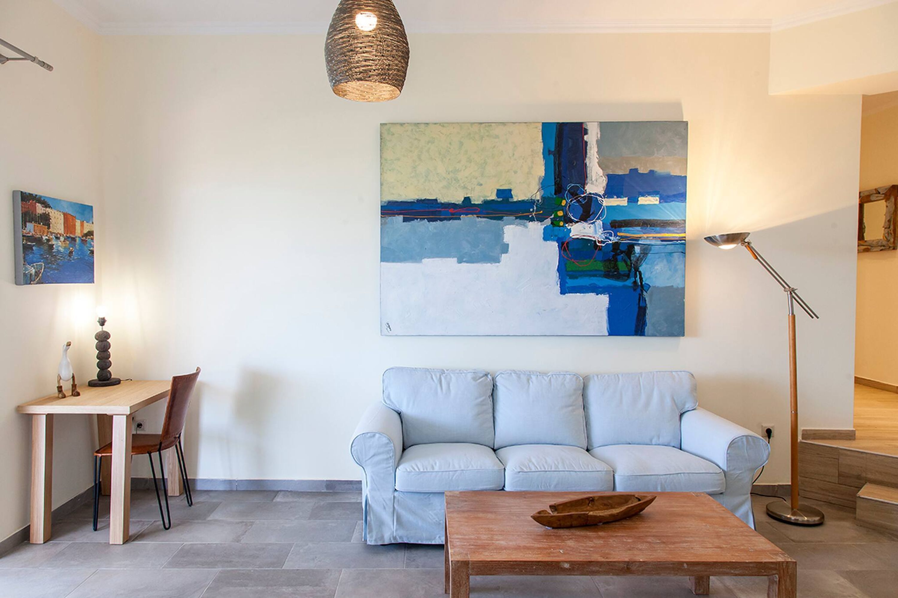 A living room with a sofa, a coffee table, a desk with a chair, and a painting on the wall.