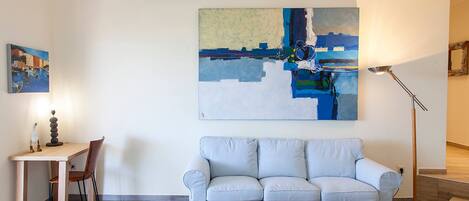 A living room with a sofa, a coffee table, a desk with a chair, and a painting on the wall.