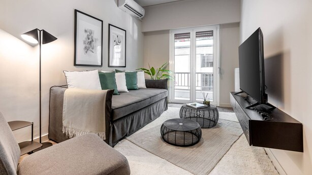 A modern living room with a sofa, two round coffee tables, a TV, and a floor lamp. - Beehive Ground in Athens (Athens)