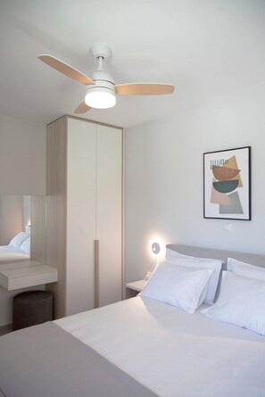 Une chambre à coucher comprenant un lit, un ventilateur de plafond, une table de chevet, une commode, un miroir et un tableau encadré accroché au mur.