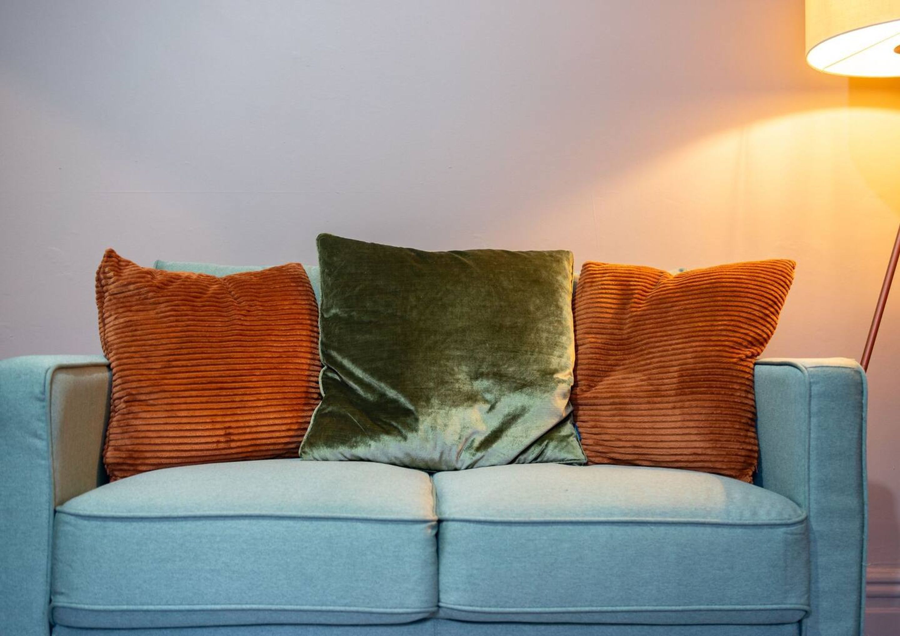 A light blue sofa with three cushions in shades of orange and green.