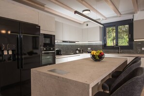 Une cuisine moderne dotée d’un grand îlot central, d’appareils électroménagers en acier inoxydable et d’une fenêtre donnant sur un paysage verdoyant.