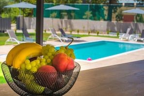 A poolside area with lounge chairs and umbrellas, a fruit bowl on a table, and a swimming pool in the background. - Villa Olia in Vasiliki (Lefkada)