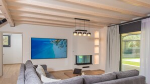Uma sala de estar moderna com um sofá cinza grande, uma TV de tela plana e teto de madeira.