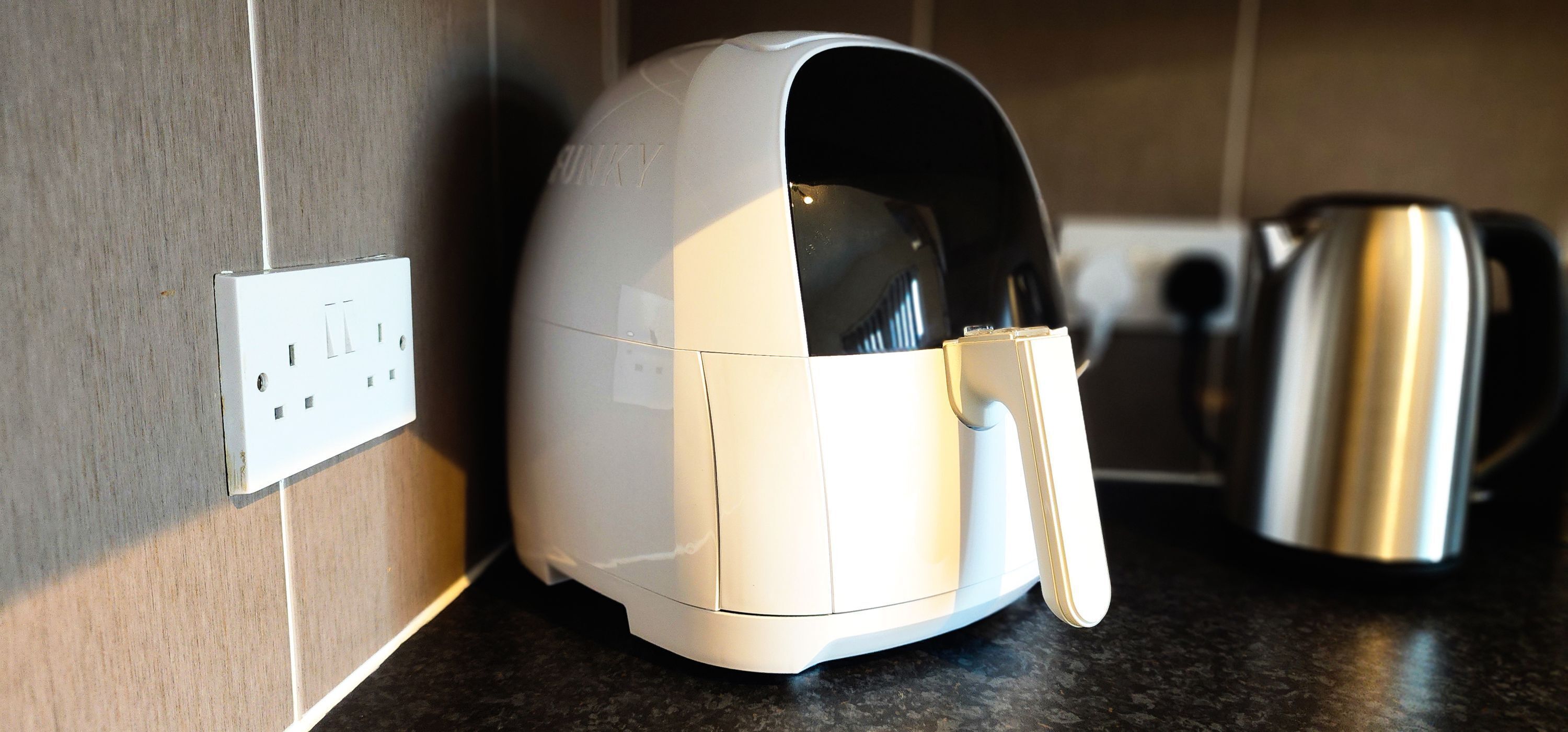 Une friteuse à air blanche est posée sur un plan de travail de cuisine, à côté d’une bouilloire.