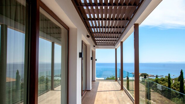 Un balcon avec vue sur la mer, de grandes portes vitrées et une pergola en bois.