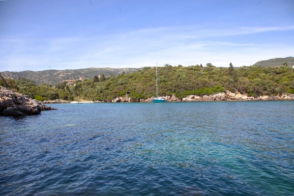 A coastal landscape with clear water, a boat, and a hilly backdrop.