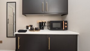 Uma cozinha compacta com micro-ondas, cafeteira e xícaras sobre o balcão.