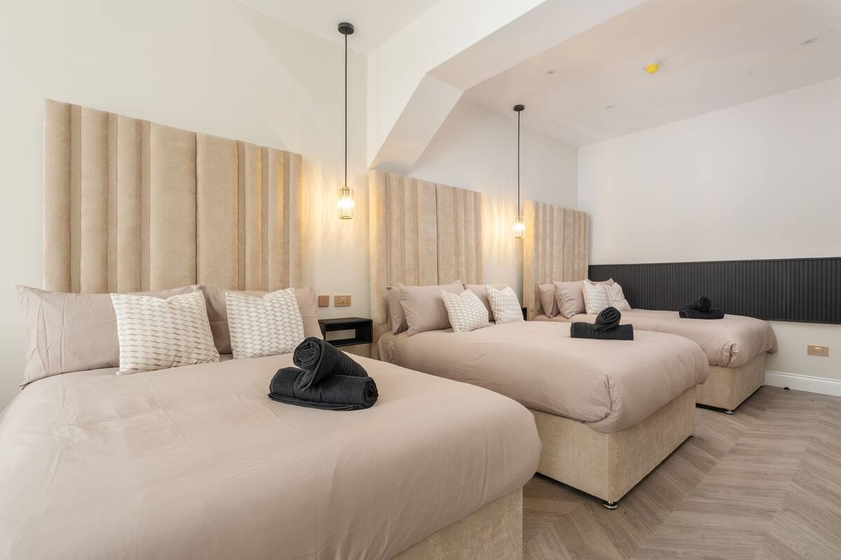Habitación de hotel con tres camas, un ventanal grande y un diseño moderno en el techo.