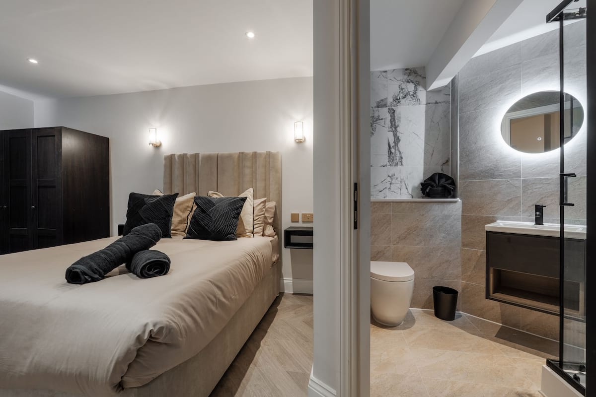 Un dormitorio moderno con cama, mesitas de noche y un baño que incluye inodoro, lavabo y espejo.