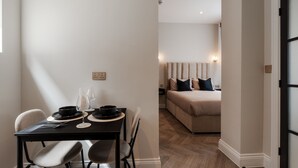 Uma sala de jantar com uma mesa, cadeiras e uma cama ao fundo.