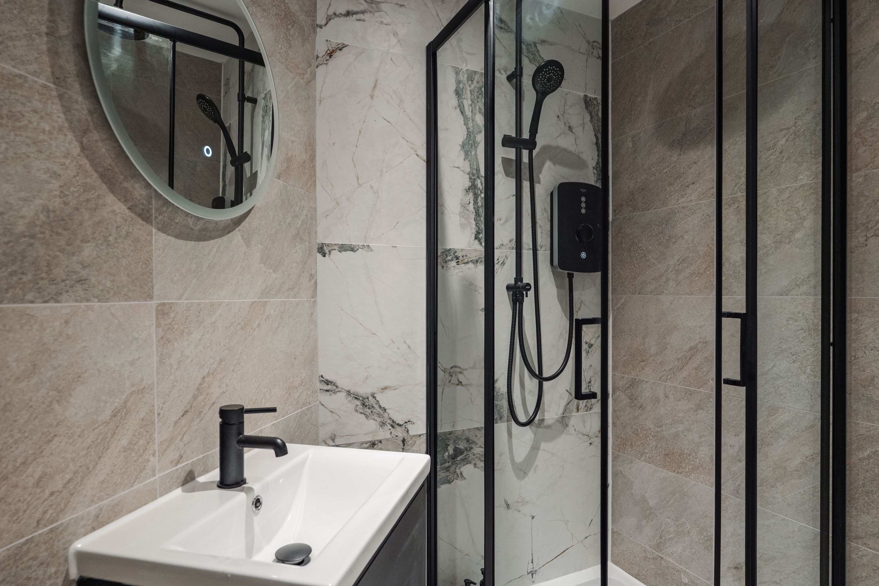 Un baño moderno con ducha de vidrio, espejo redondo y lavamanos blanco.