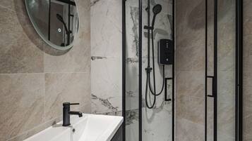 Un baño moderno con ducha de vidrio, espejo redondo y lavamanos blanco.