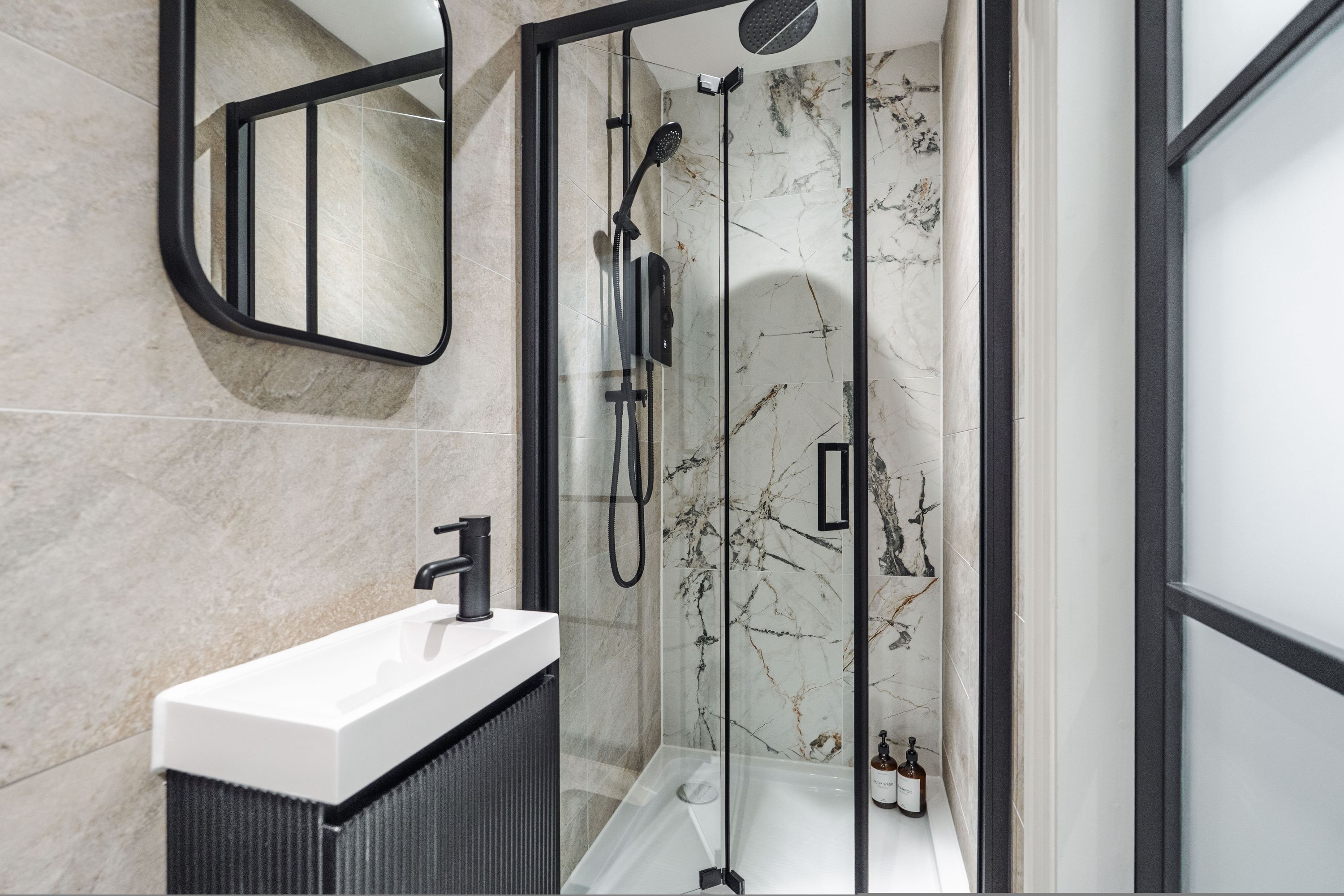 Un baño moderno con ducha envuelta en vidrio, un lavabo blanco y paredes de mármol.