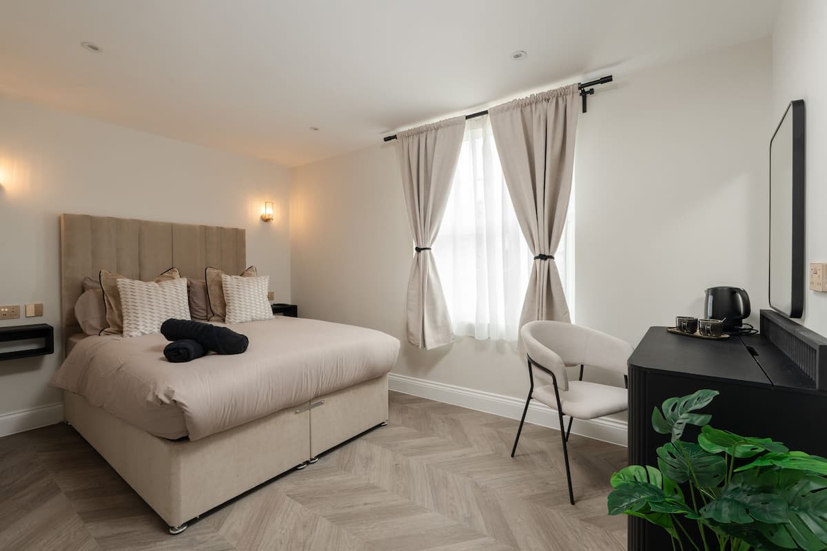 Un dormitorio con cama, mesitas de noche, una silla, un escritorio y una planta en maceta.