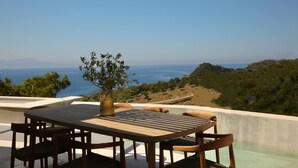 A wooden table with chairs on a terrace overlooking a body of water and hills. - Scirocco Penelope 2 BED (Lefkada)