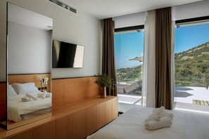 Habitación de hotel con cama, un espejo grande, televisor de pantalla plana, mesita de noche de madera, planta en maceta y balcón con vista a una colina.