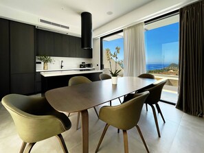 A modern kitchen with dark cabinetry, a central island, and a dining area with a large table and chairs.