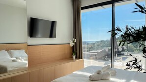A modern hotel room with a large bed, a flat-screen TV, a potted orchid, and a view of the cityscape. - Scirocco Penelope 2 BED (Lefkada)