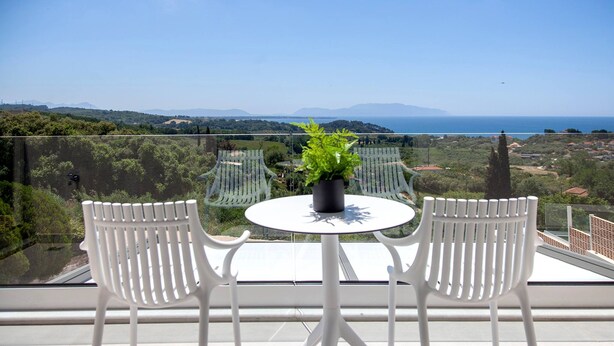 Un balcón con dos sillas blancas y una mesa, con vistas a un paisaje pintoresco con montañas y el mar.