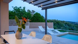 Un patio moderno al aire libre con piscina, sillas blancas, una mesa y una planta decorativa.