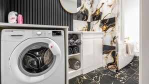 A modern bathroom with a built-in washing machine, marble wall tiles, and a mirror. - Anfield 3 Mins Superfast Wifi Washer Sofabed (Liverpool)