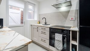 A modern kitchen with a built-in oven, a stainless steel range hood, and a window with blinds. - Anfield 3 Mins Superfast Wifi Washer Sofabed (Liverpool)