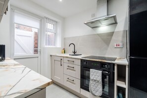 A modern kitchen with a built-in oven, a stainless steel range hood, and a window with blinds. - Anfield 3 Mins Superfast Wifi Washer Sofabed (Liverpool)