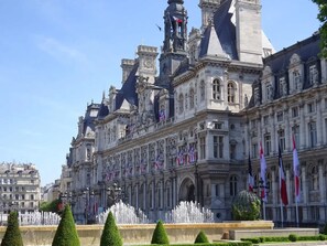 A historic building with classical architecture, a fountain, and flags. - Historic Parisian Gem Chic Central Retreat (Paris)