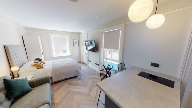 Et moderne, lyst værelse med seng, sofa, spisebord og et fjernsyn ophængt på væggen.