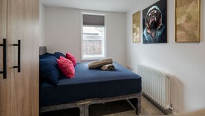 Ein Schlafzimmer mit Bett, Kissen, Heizkörper, Fenster und Bildern an der Wand.