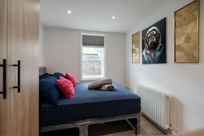 Ein Schlafzimmer mit Bett, Kissen, Heizkörper, Fenster und Bildern an der Wand.