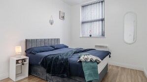 A bedroom with a bed, bedside table, lamp, window with blinds, and a mirror. - Smart TV W M With Sofa Bed Free Parking (Liverpool)