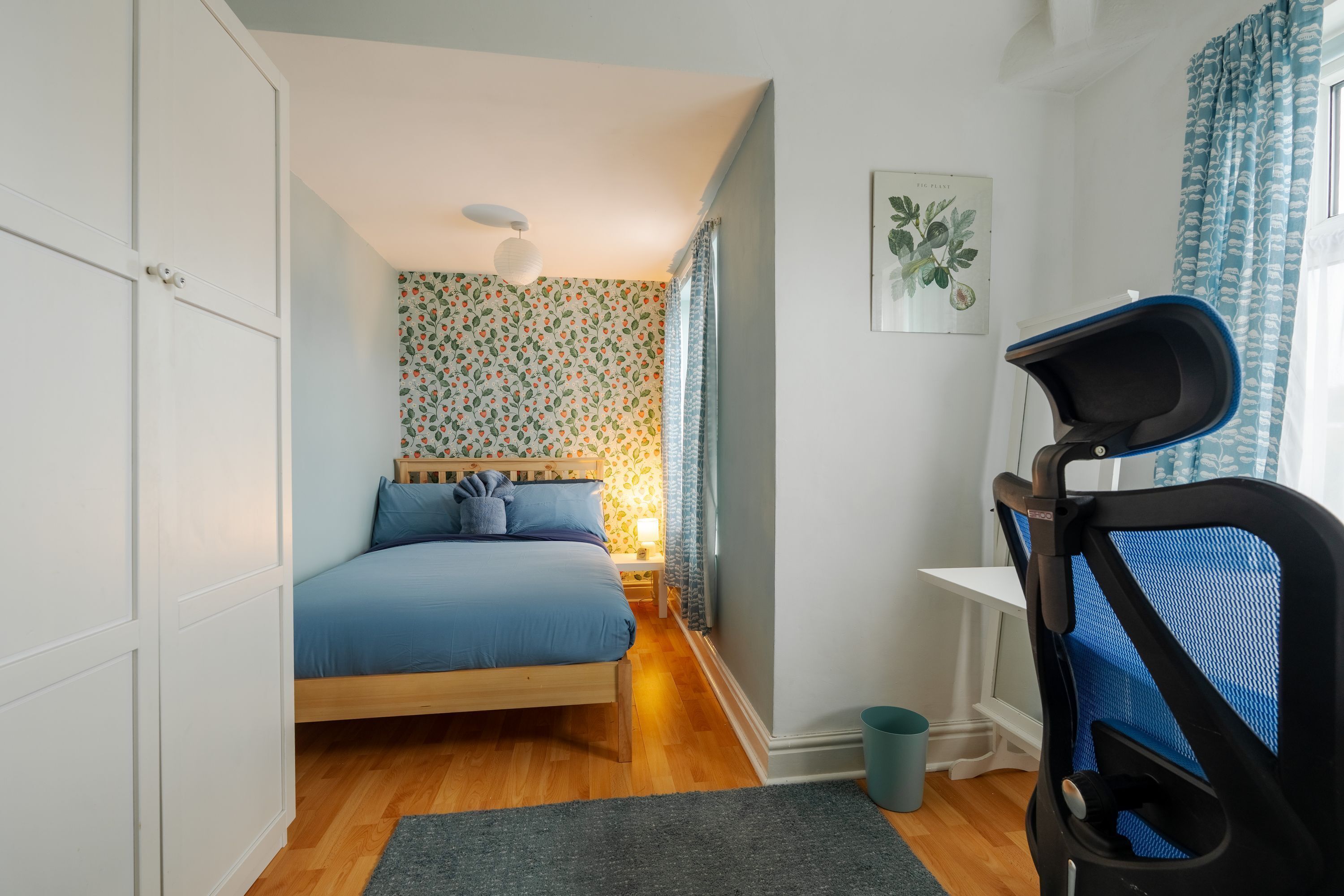 Une chambre à coucher comprenant un lit, un bureau, une chaise, une étagère fixée au mur et une fenêtre avec des rideaux.