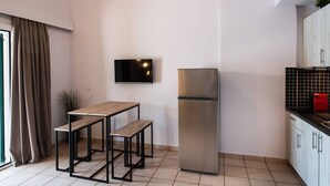 A modern kitchen with a built-in refrigerator, a wooden table with benches, a flat-screen TV mounted on the wall, and a window with curtains. - Drakatos X Apartment (Lefkada)