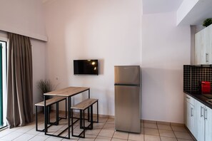 A modern kitchen with a built-in refrigerator, a wooden table with benches, a flat-screen TV mounted on the wall, and a window with curtains. - Drakatos X Apartment (Lefkada)