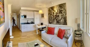 A modern living space with a kitchen, dining area, and a sofa with red cushions. - Apartment Near Monaco Rolex Masters (Roquebrune-Cap-Martin)