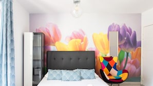 Un dormitori modern amb un llit, una cadira colorida, un armari i una paret amb un mural floral.