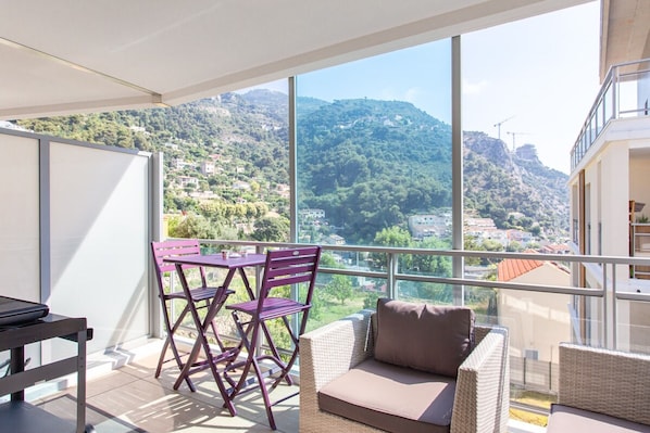 A balcony with a view of a mountainous landscape, a wicker sofa, and a table with chairs. - Studio Cosy et Moderne 5 min de Monaco (Beausoleil)