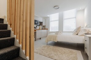 Quarto com cama, mesa de cabeceira e vista para a cozinha.